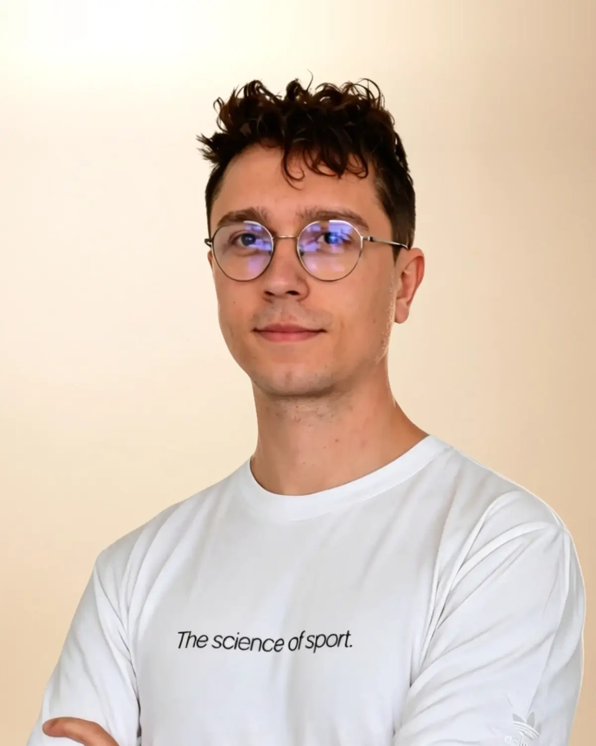 Dominik Budny, fizjoterapeuta i trener personalny, w białej koszulce, w okularach, z założonymi rękami