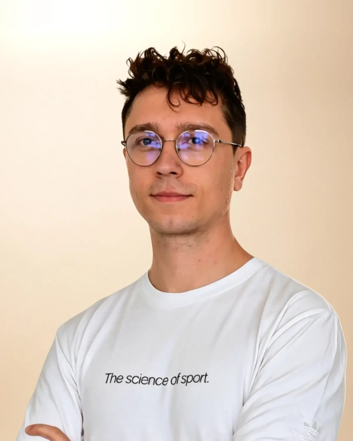 Dominik Budny, fizjoterapeuta i trener personalny, w białej koszulce, w okularach, z założonymi rękami