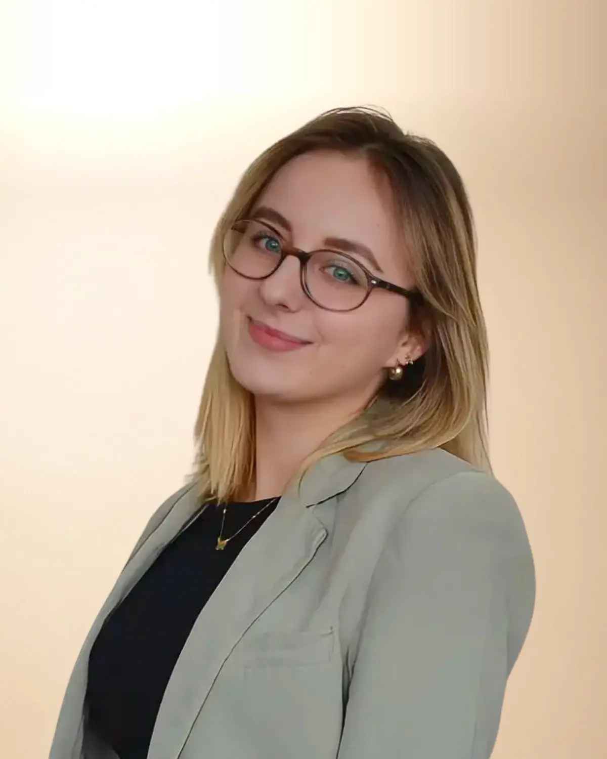 Martyna Basiewicz, logopeda i pedagog specjalny, w szarozielonej marynarce i okularach, uśmiechnięta