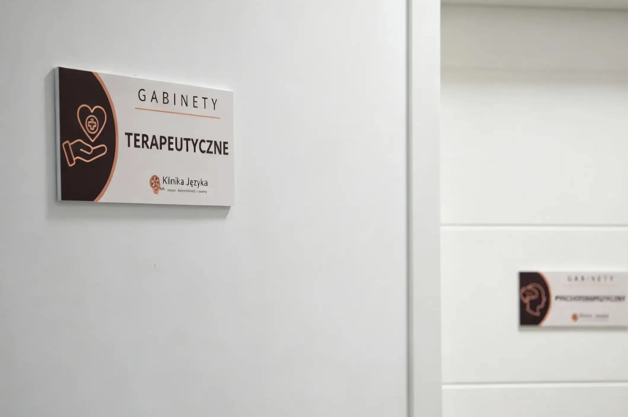 Tabliczka na drzwiach z napisem Gabinety terapeutyczne i logo Kliniki Języka